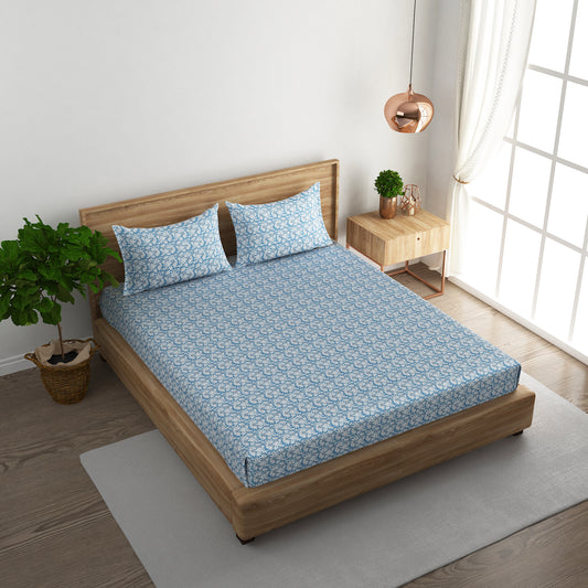 Bed with blue floral bedding in a bright room with a plant and side table.